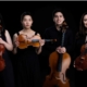 Asaka Quartet stood holding string instruments. The are stood against a black back drop