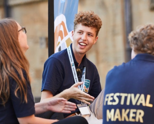 A group of Festival Makers sat together talking and laughing. They were black T shirts with Festival Maker in gold print and Southwell Music Festival lanyards.