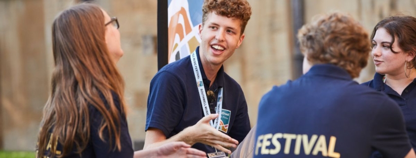 A group of Festival Makers sat together talking and laughing. They were black T shirts with Festival Maker in gold print and Southwell Music Festival lanyards.