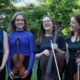 Four young string players stood together outside holding their instruments and laughing.