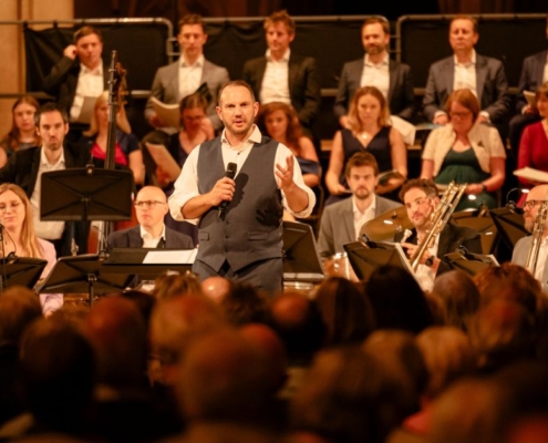 Marcus Farnsworth introducing a concert in Southwell Minster. He stands in front of a big band and holds a microphone in his hand.