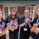 Four Festival Makers stood tofether outside the Trebeck Hall, holding Festival merchandise and programme books